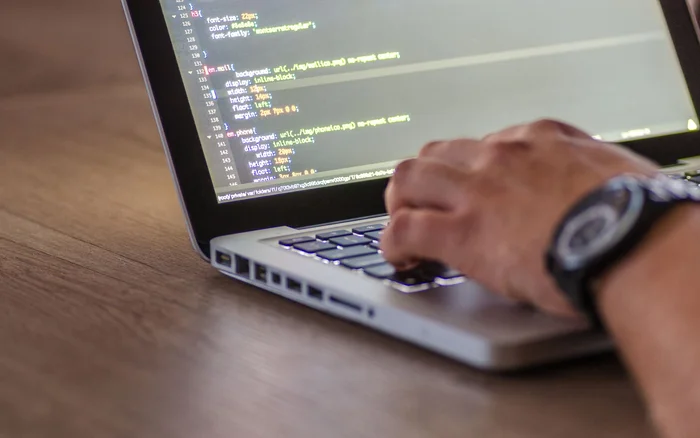 Hands working on a laptop displaying code