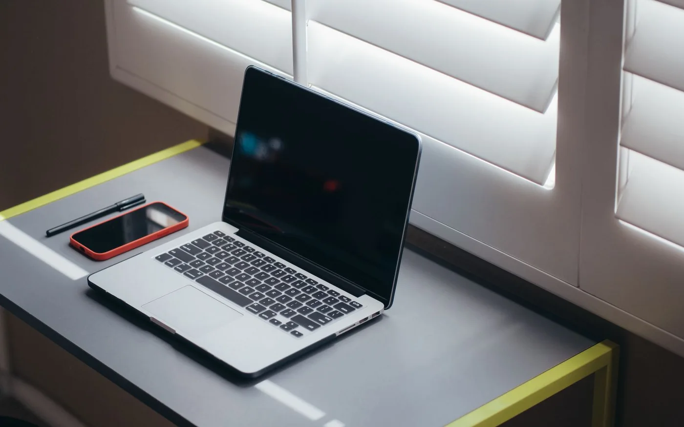 Laptop, smartphone, and pen on a softly lit desk